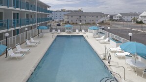 A swimming pool with lounge chairs and umbrellas, surrounded by a building with multiple balconies. - Dunes Court (Ocean City)