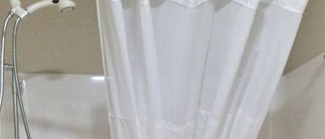 A shower area with a white curtain, a towel rack, and a small shelf with folded towels.