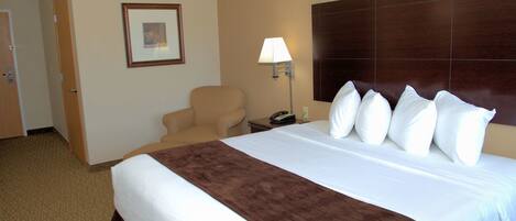 Habitación de hotel con una cama grande, una silla, una lámpara y un cuadro en la pared.