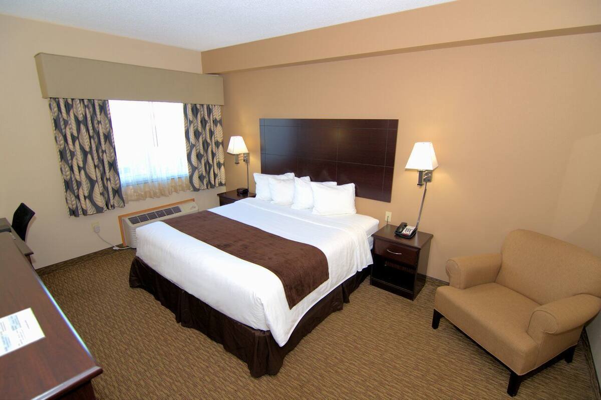 A hotel room with a large bed, two bedside lamps, a chair, a desk, and a window with patterned curtains.