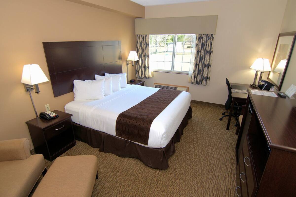 A hotel room with a large bed, two bedside tables with lamps, a desk with a chair, and a window with curtains.