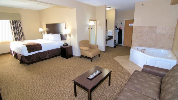 A hotel room with a bed, a chair, a sofa, a coffee table, a desk, a lamp, a mirror, a bathroom with a bathtub, and a shower. - Rock Island Inn & Suites (Atlantic)