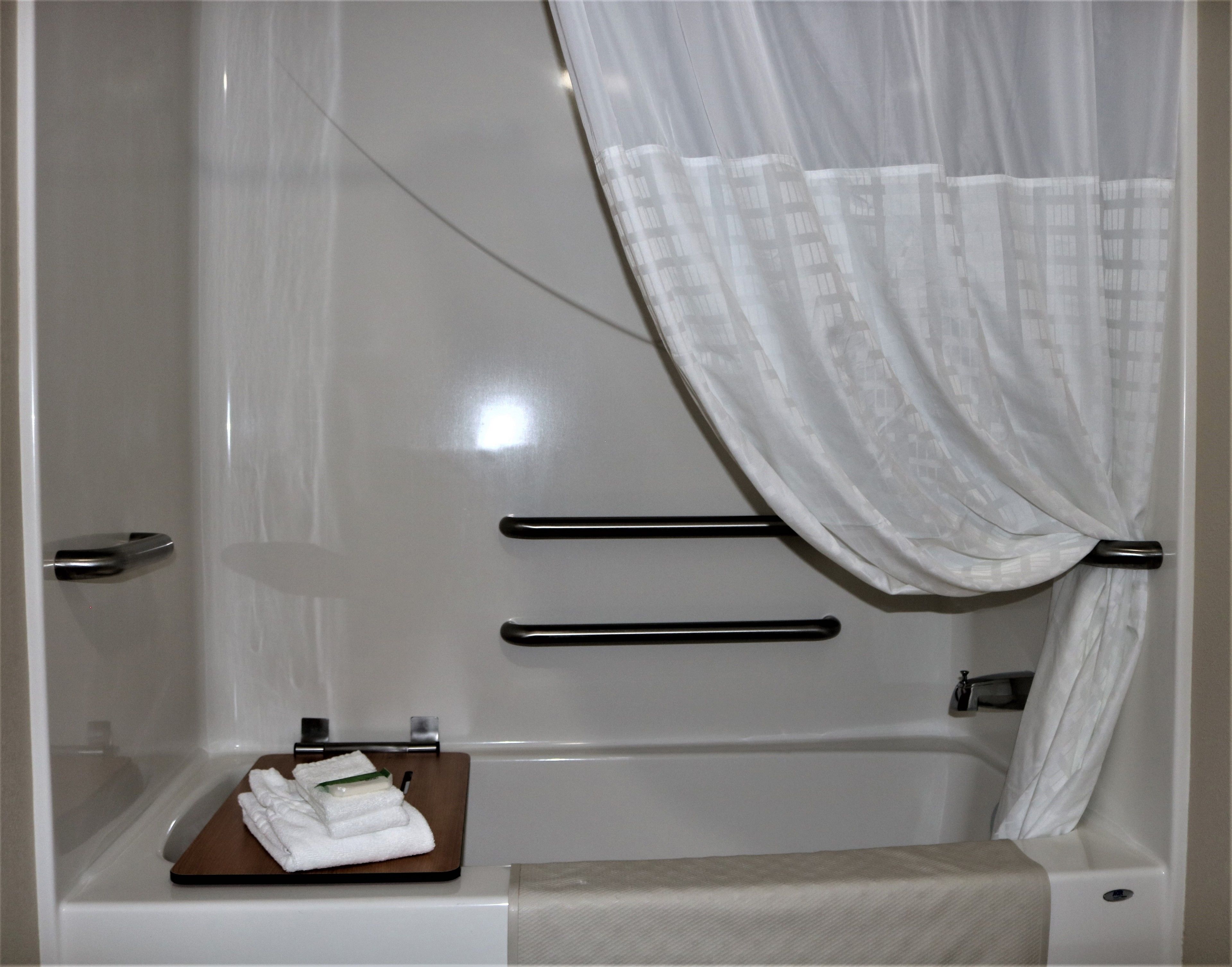 Un baño moderno con cabina de ducha de vidrio, un perchero y una bandeja de madera con toallas dobladas.
