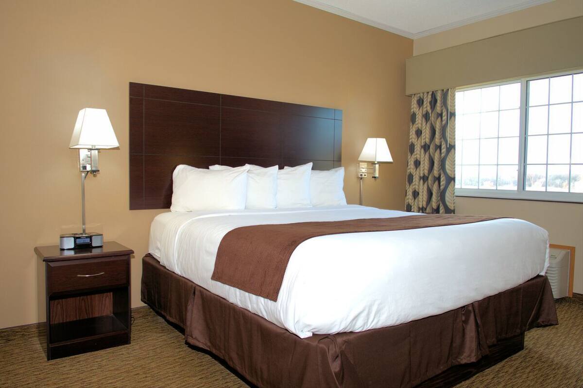 A hotel room with a large bed, two bedside lamps, a nightstand, and a window with curtains.