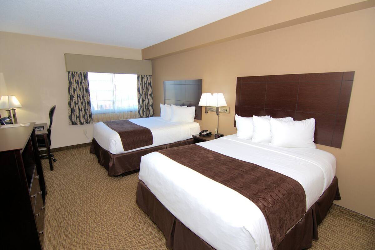 A hotel room with two beds, a desk, and a chair.