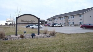 A Rock Island Inn & Suites with a parking lot and a building with multiple windows and a stone facade. - Rock Island Inn & Suites (Atlantic)