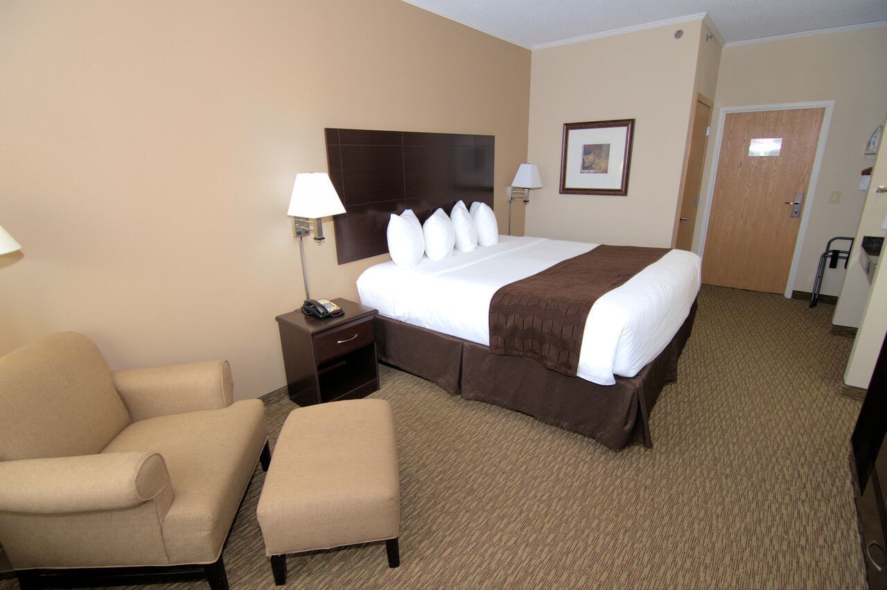 A hotel room with a large bed, a bedside table with a lamp, a chair, and a small table with a phone.
