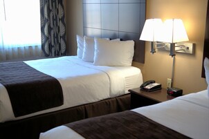 Una habitación de hotel con dos camas, una lámpara de noche, un teléfono y un reloj en la mesita de noche.