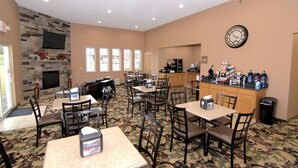 A hotel lobby with a stone fireplace, multiple tables and chairs, a clock, and a coffee station. - Rock Island Inn & Suites (Atlantic)