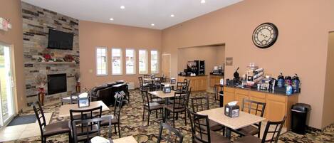 A hotel lobby with a stone fireplace, multiple tables and chairs, a clock, and a coffee station.