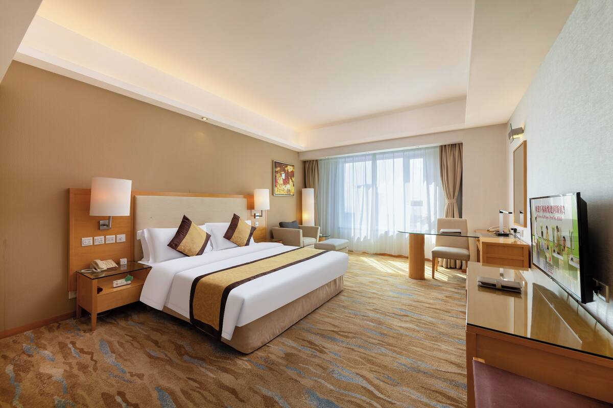 Hotelkamer met een groot bed, nachtkastjes, een bureau, een stoel, een televisie en een raam met gordijnen.