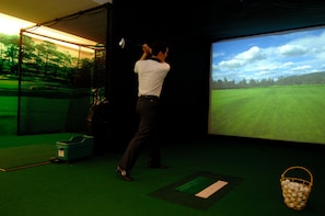 A man playing golf indoors with a large screen displaying a golf course.