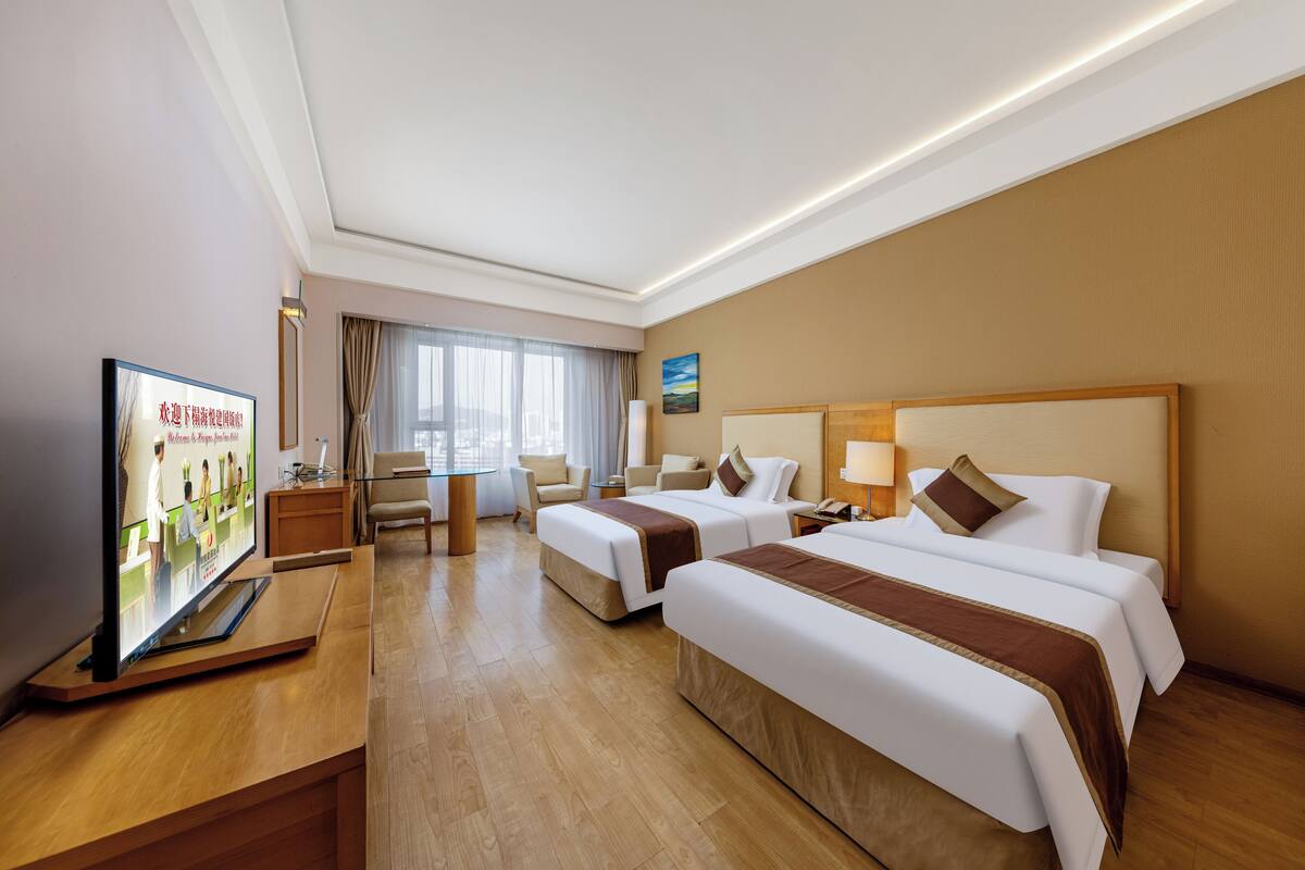 Een hotelkamer met twee bedden, een bureau, een televisie en een raam met gordijnen.