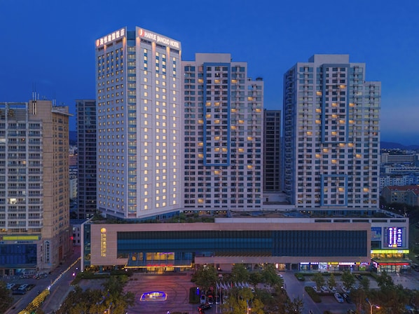A modern hotel complex with multiple high-rise buildings, a central building with large glass windows, and a well-lit parking area.