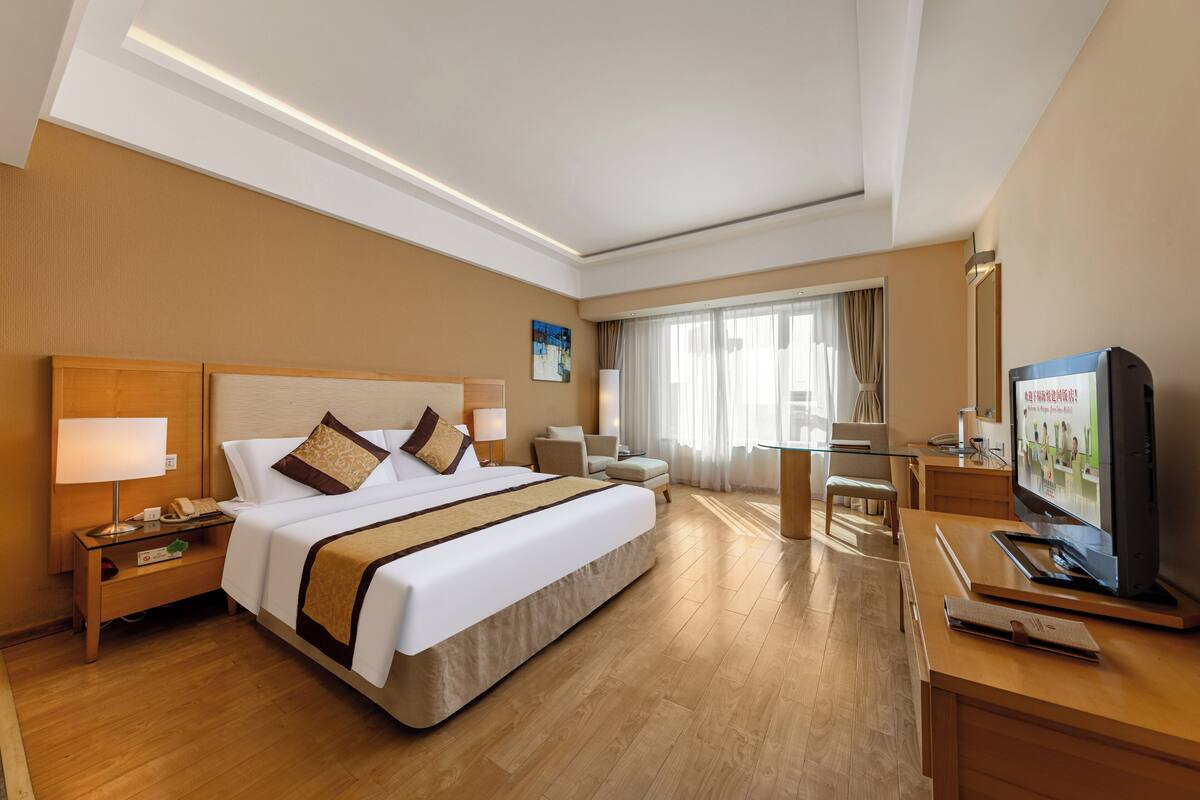 Een hotelkamer met een groot bed, nachtkastjes, een bureau met een televisie en een raam met gordijnen.