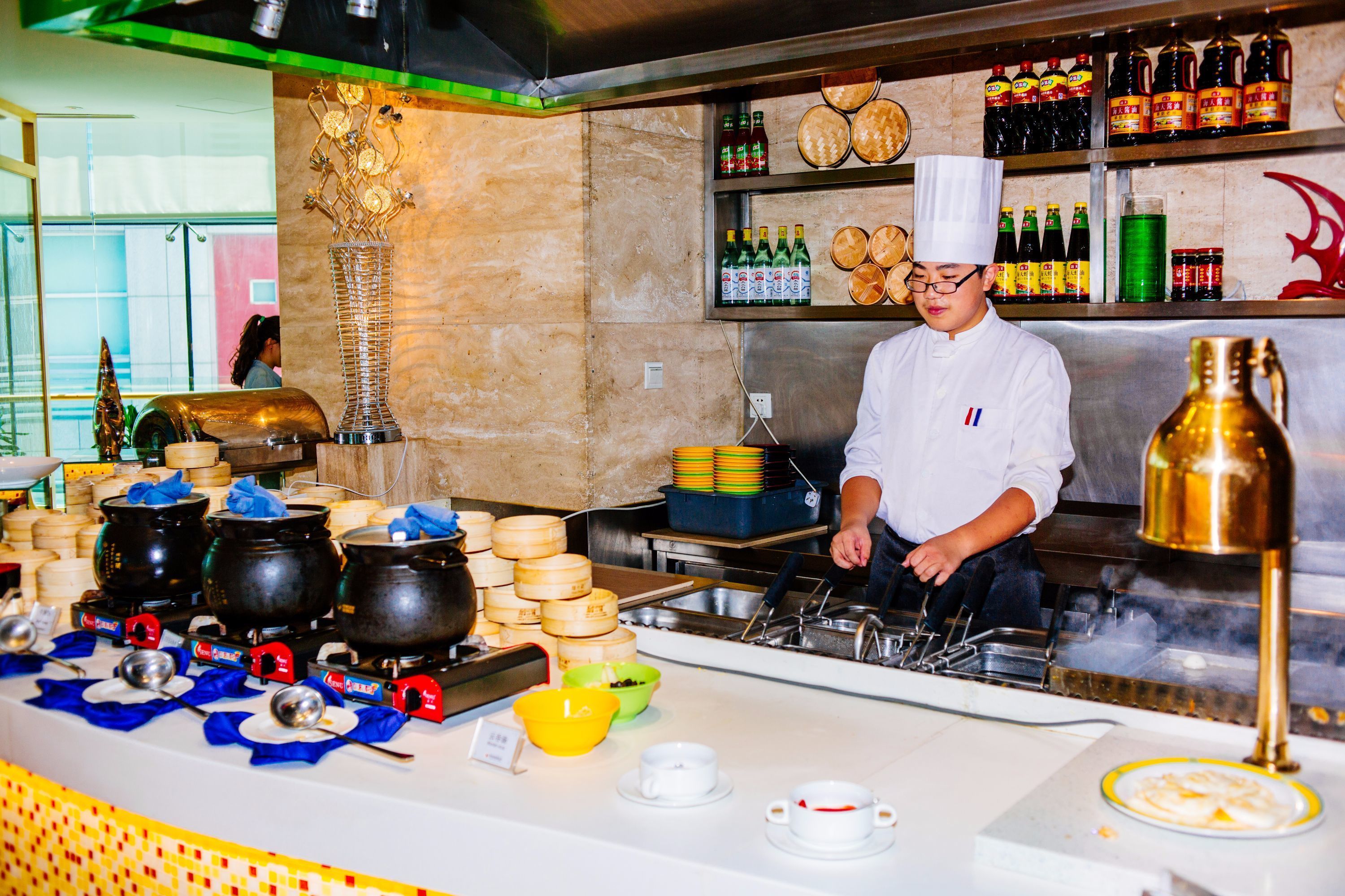 A chef preparing food in a kitchen with various cooking utensils, pots, and a display of condiments.