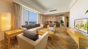 A modern hotel room with a sofa, armchair, and coffee table, a TV, and a view of the city.