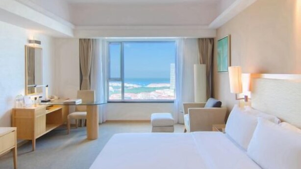 A hotel room with a large bed, a desk, a chair, a small table, and a view of the beach.