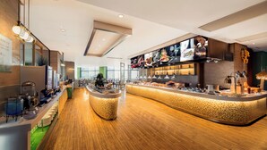 A modern restaurant with a central buffet area, wooden flooring, and a variety of food displays.