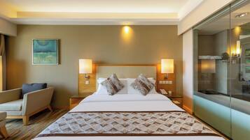 Une chambre d’hôtel avec un grand lit, deux lampes de chevet, une chaise, un tableau au mur et une cabine de douche en verre.