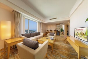 A modern hotel room with a sofa, armchair, and coffee table, a TV, and a view of the city.