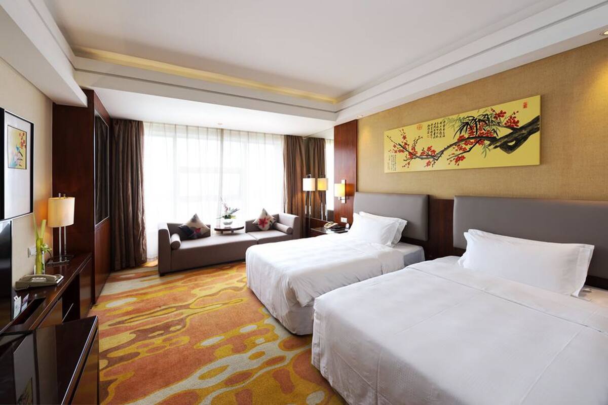 Une chambre d’hôtel avec deux lits, un canapé, un bureau et un grand tableau au mur.