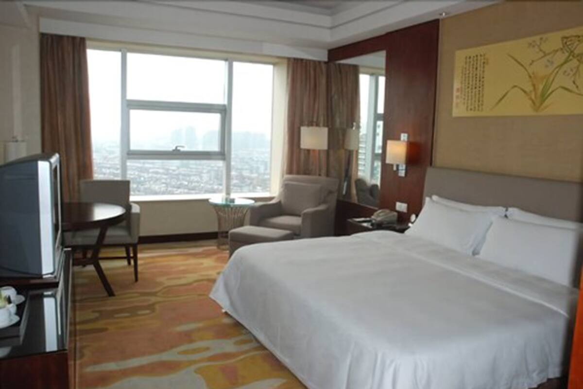 Une chambre d’hôtel avec un grand lit, un bureau, une chaise, une télévision et une vue sur la ville par la fenêtre.