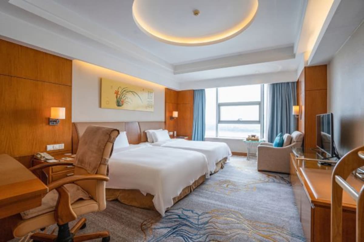 Habitación de hotel con dos camas, un escritorio, una silla, un televisor y un ventanal con cortinas.