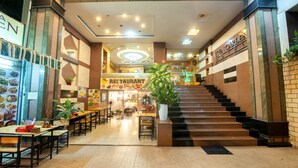 Eine Hotelhalle mit einer Treppe zum Obergeschoss, einem Restaurantbereich und einer Rezeption.