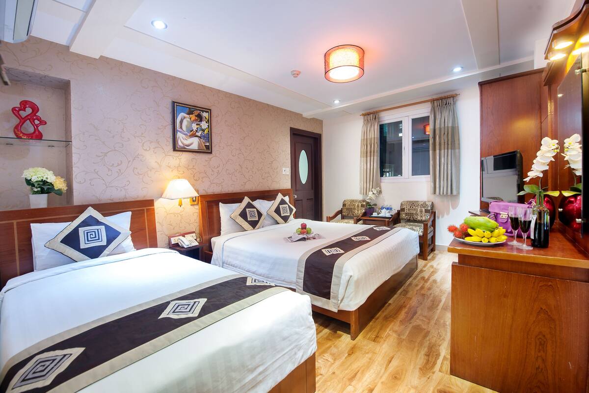 Ein Hotelzimmer mit zwei Betten, einem Schreibtisch mit Obstschale, einem Spiegel und einem Fenster mit Vorhängen.