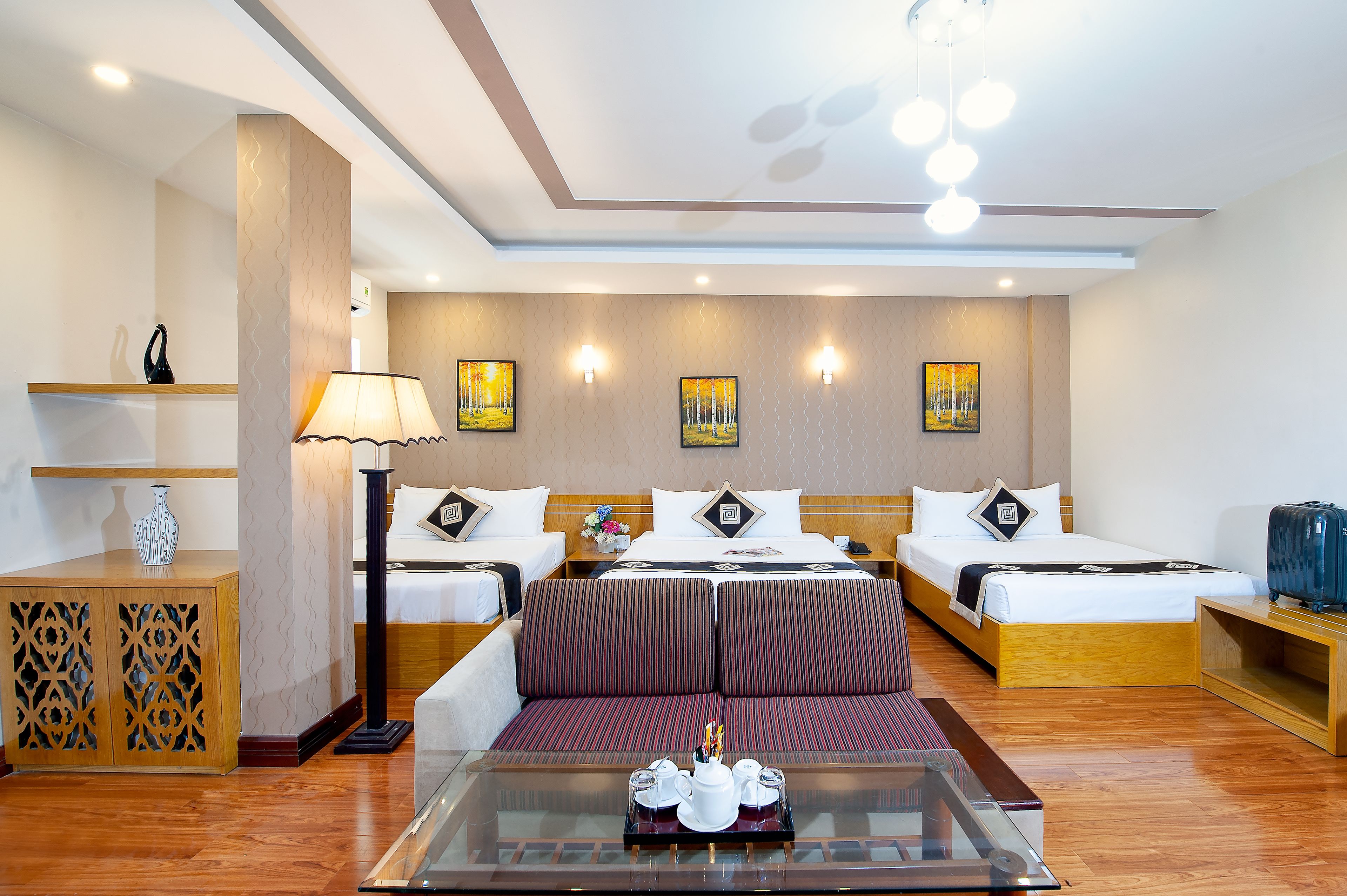 A hotel room with two beds, a glass coffee table, a wooden cabinet, and wall-mounted artwork.