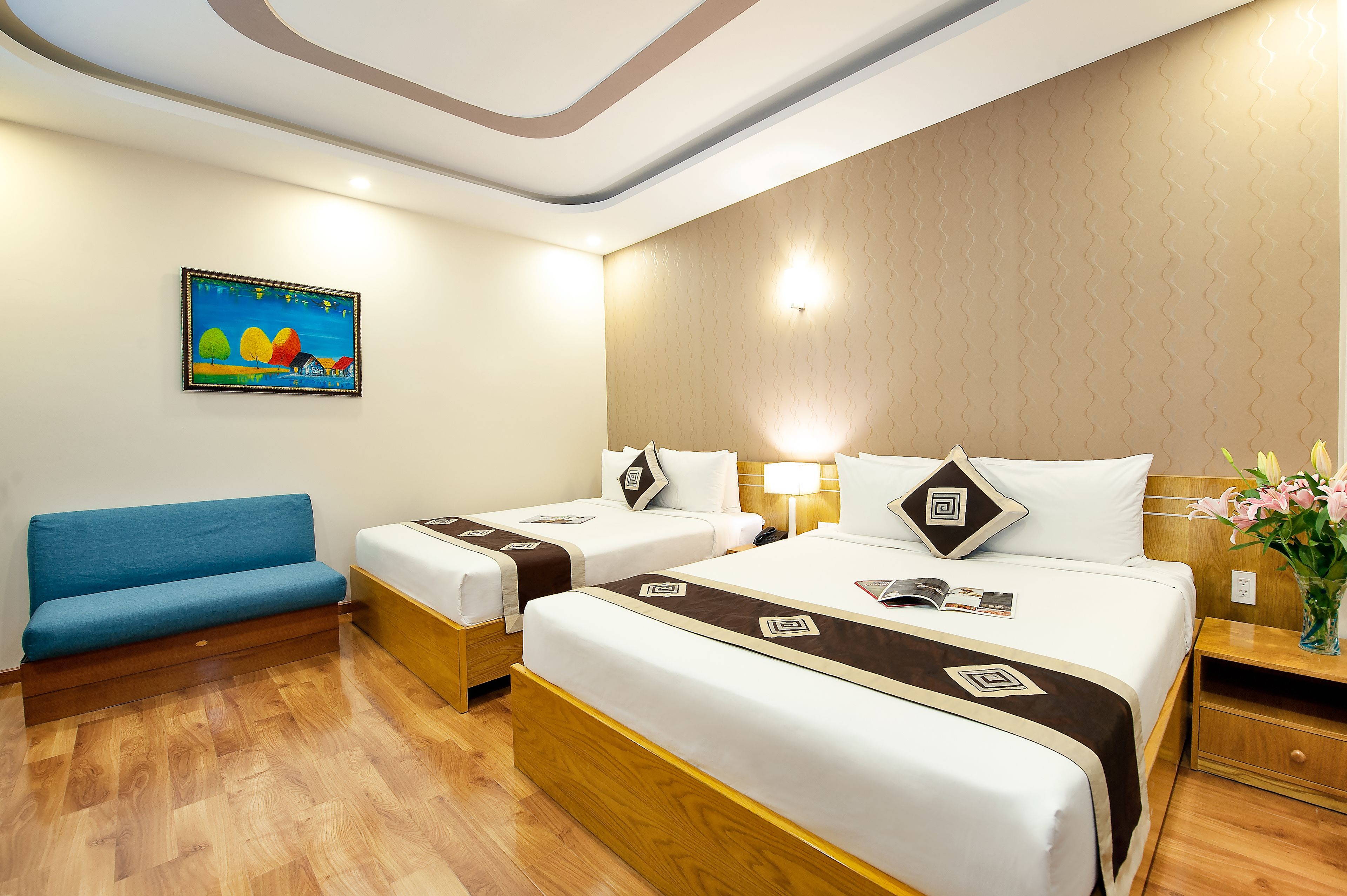 Habitación de hotel con dos camas, un sofá azul, un cuadro en la pared y suelo de madera.