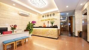 Een hotel receptie met een marmeren balie, een receptiemedewerker en een zithoek met banken.