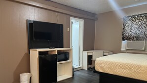 Una habitación de hotel pequeña con una cama, un televisor sobre un soporte de madera, un escritorio y un armario.