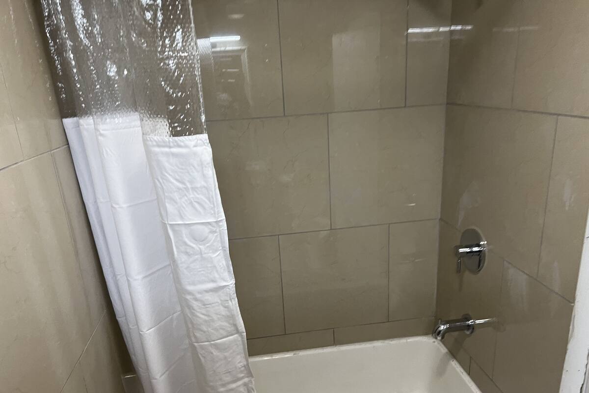 Une petite cabine de douche carrelée avec un rideau blanc.