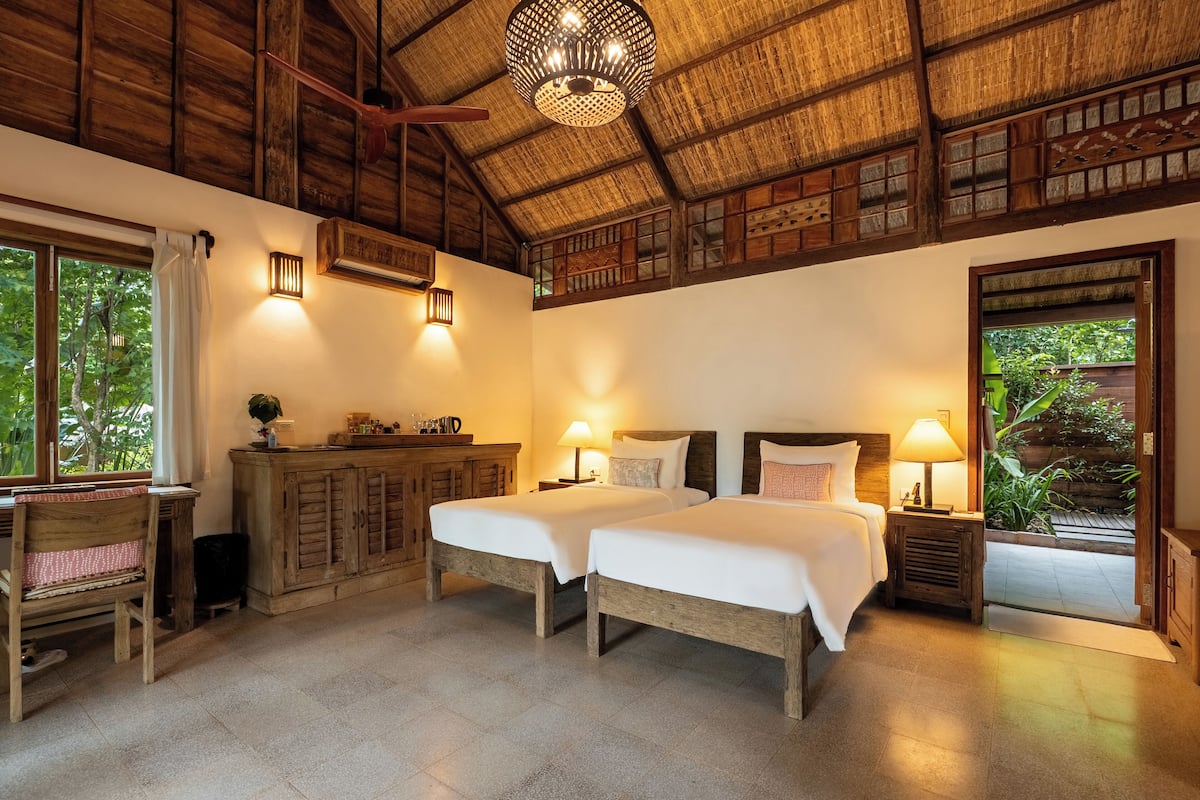 A room with two beds, wooden furniture, and a thatched roof ceiling.
