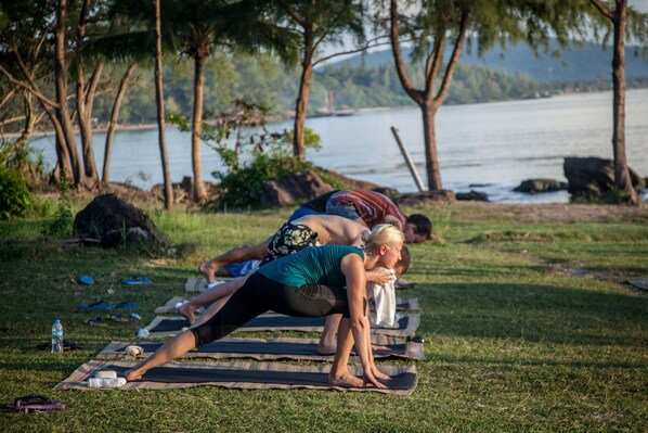 A group of people doing yoga on mats in an outdoor setting with a lake and trees in the background.