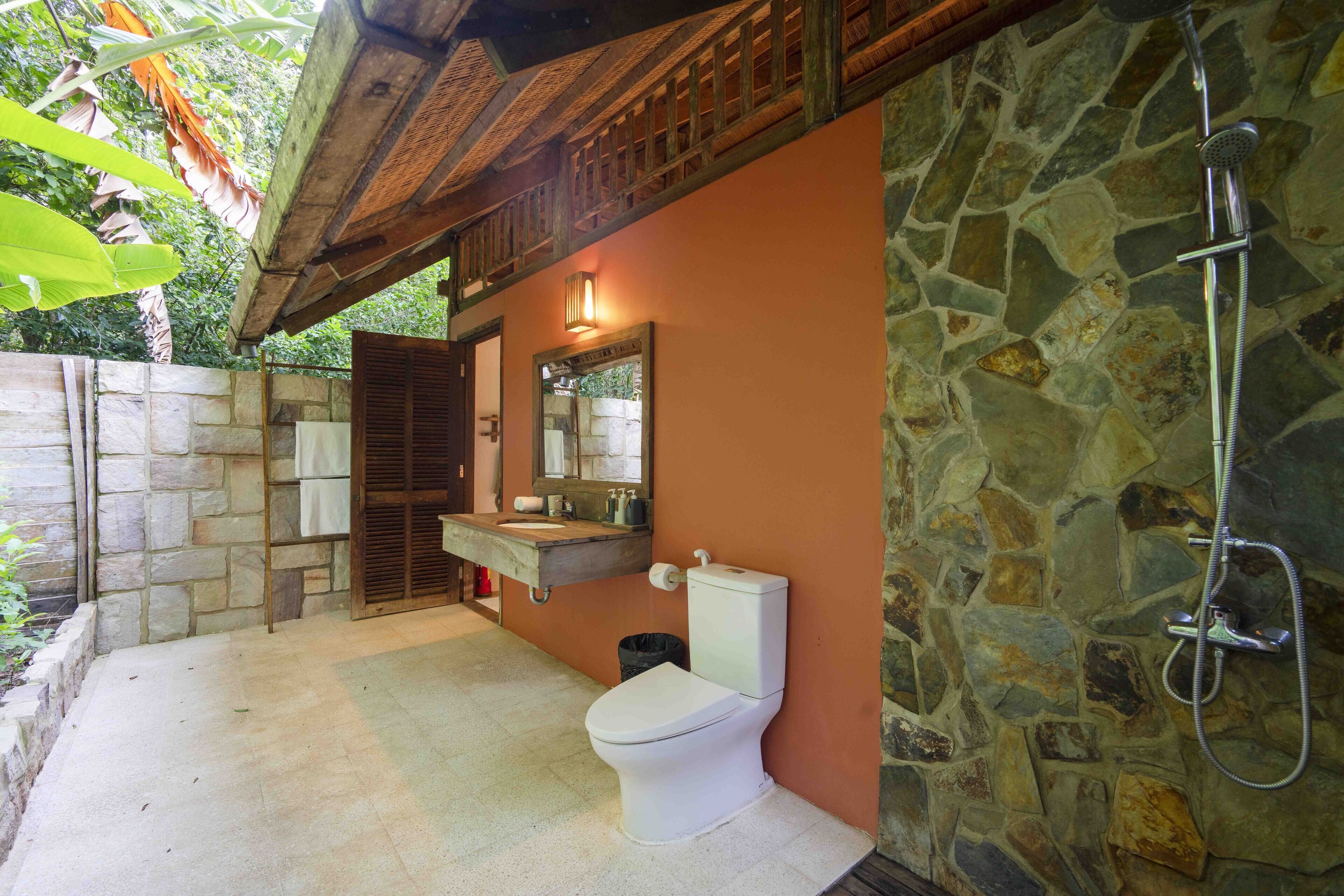Un baño con ducha de piedra, inodoro blanco y tocador de madera con espejo.