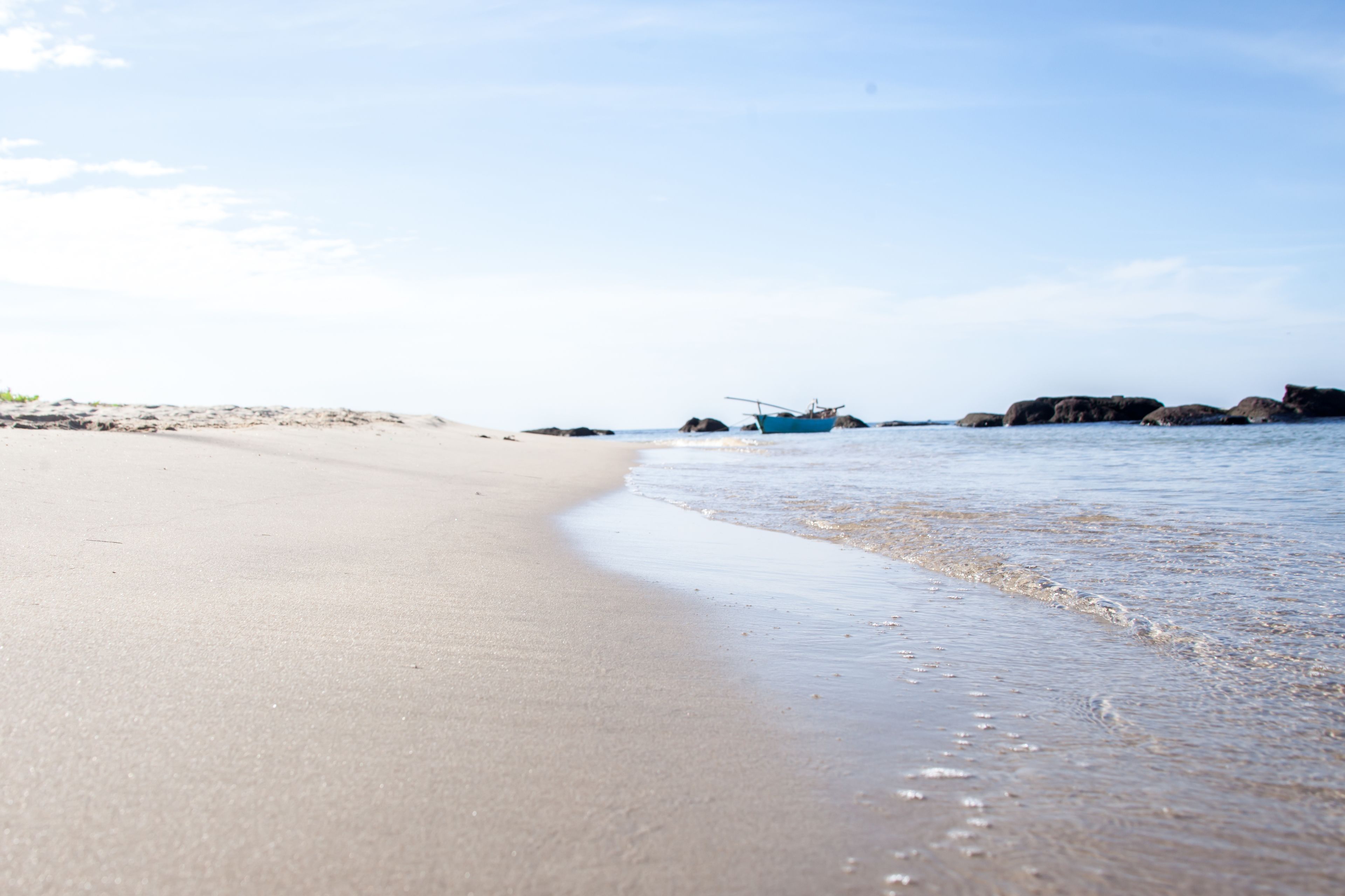 Una playa con un bote y rocas a lo lejos.