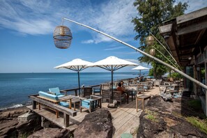 A wooden deck with outdoor seating, white umbrellas, and a view of the sea.