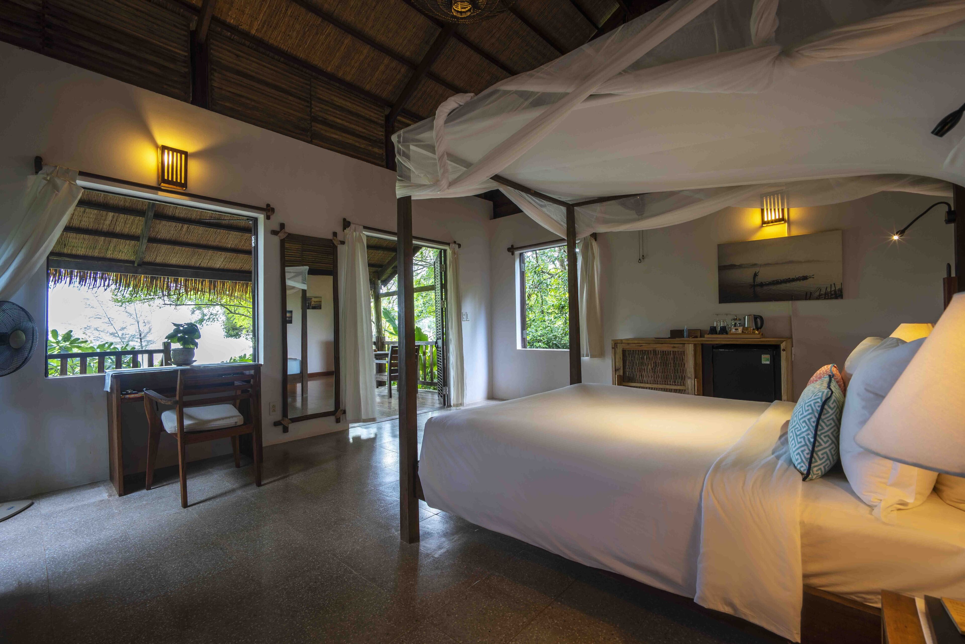 A bedroom with a bed, bedside table, lamp, and a view of the outdoors.