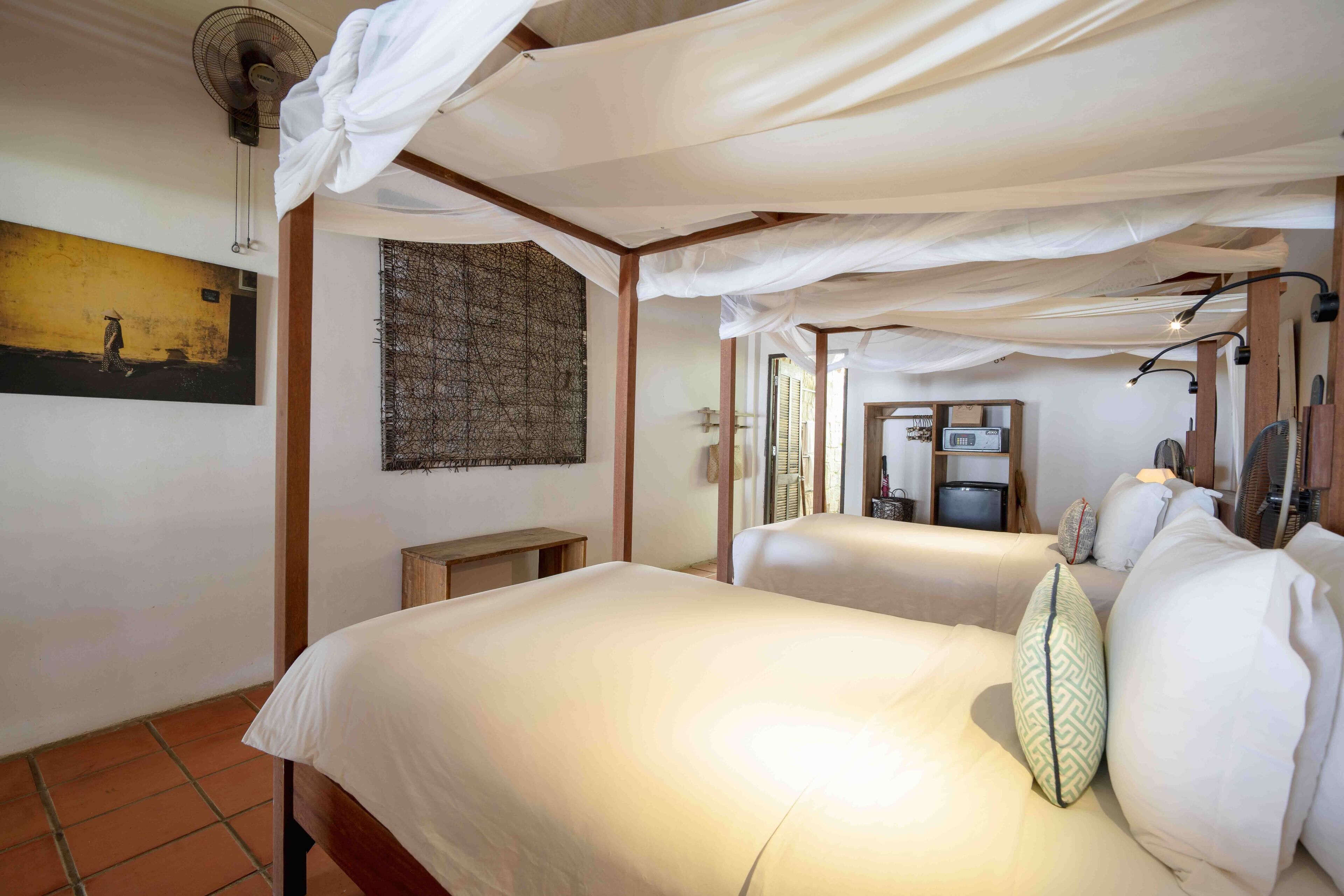 A room with two beds, a wooden bench, a wall-mounted fan, and a framed picture.