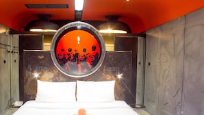 Habitación de hotel con una cama, dos almohadas, un espejo redondo y dos toallas enrolladas.
