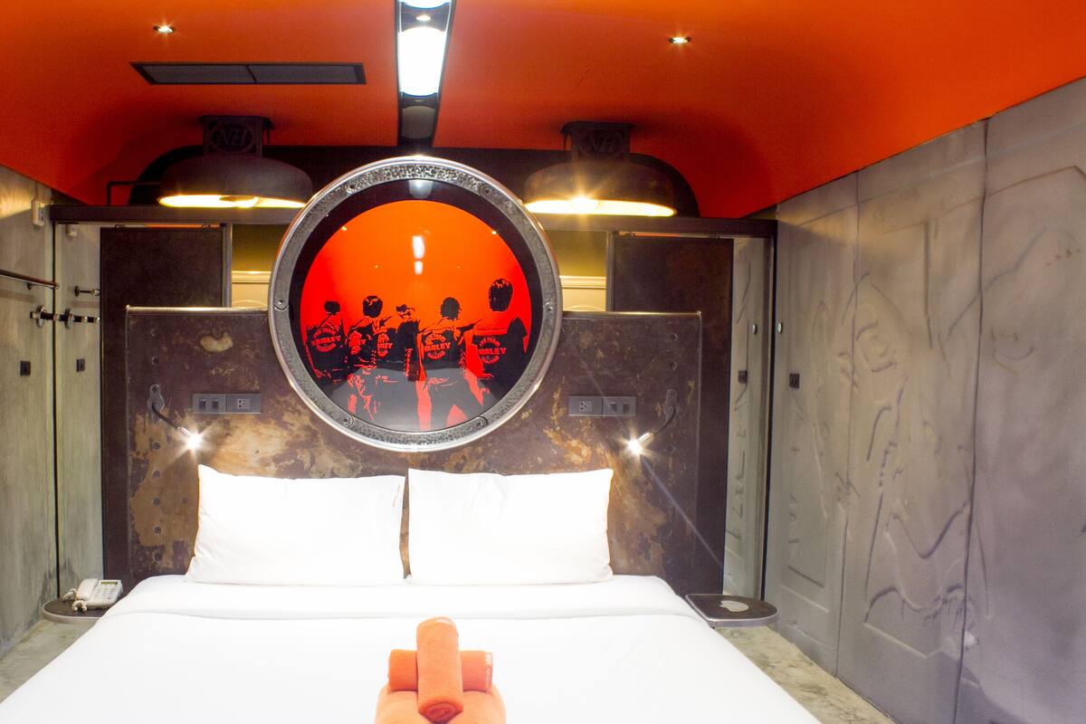 A hotel room with a bed, two pillows, a round mirror, and two rolled towels.