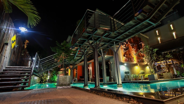 Vista nocturna de un hotel moderno con piscina, asientos al aire libre y una escalera que conduce a la entrada.