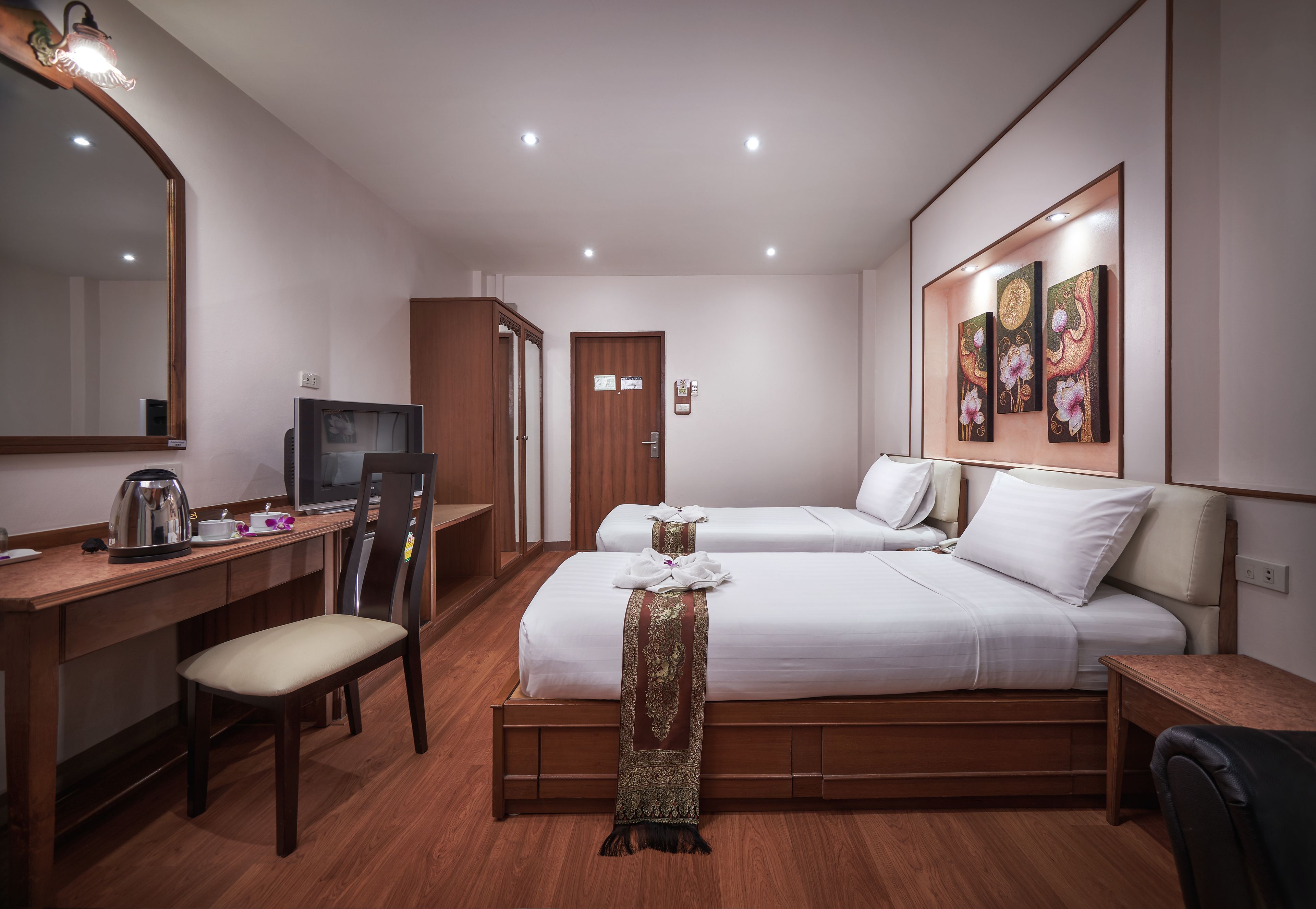 Une chambre d’hôtel avec deux lits, un bureau avec une télévision, une chaise et un grand miroir.