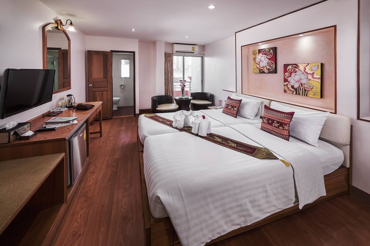 A hotel room with a large bed, a desk with a TV, and two chairs.