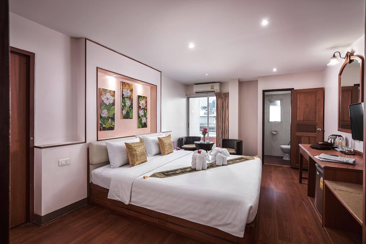 A hotel room with a large bed, a desk with a chair, a bathroom, and a view of the city.