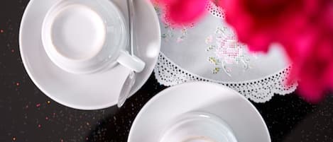 A black tray with two white cups and saucers, a spoon, and a lace doily with a pink rose.