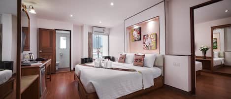 A hotel room with a large bed, a desk with a chair, a wardrobe, and a bathroom visible through an open door.